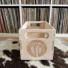 Baltic birch wood 7″ vinyl crate showing laser‑engraved cobra logo on one side, placed on a cowhide rug with vinyl records in the background.