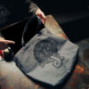 Hand holding a gray Snake Park Records canvas tote filled with 12" vinyl records on a rustic metal table.