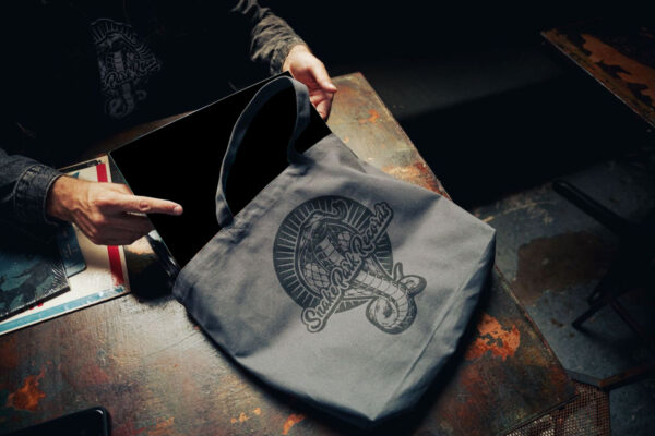 Hand holding a gray Snake Park Records canvas tote filled with 12" vinyl records on a rustic metal table.