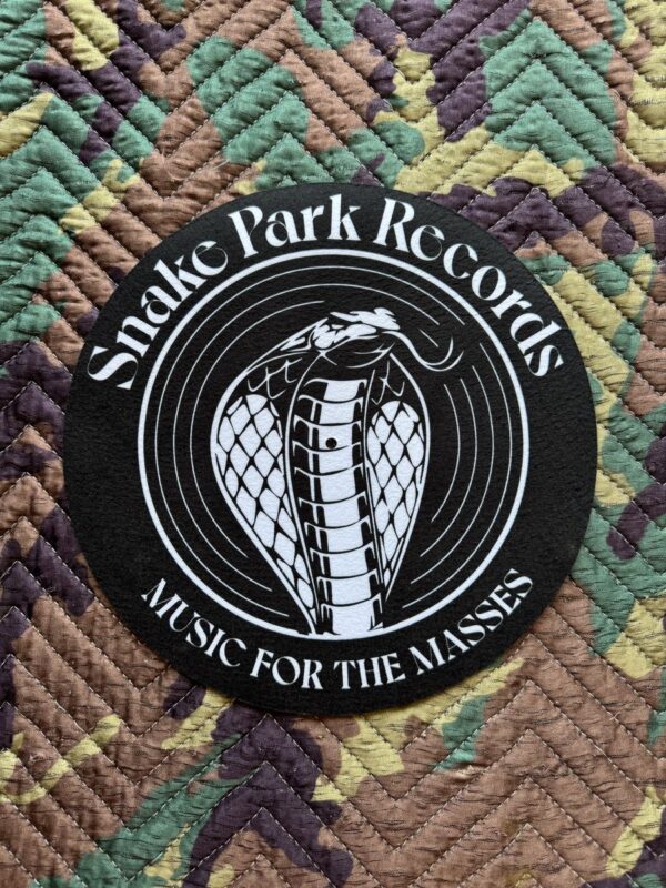 Overhead close‑up of a black Snake Park Records slipmat showing a white cobra logo and “Music for the Masses” text on a multicolored quilted background.