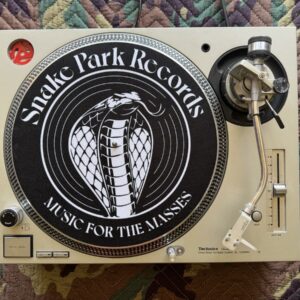 Top‑down view of a Technics SL‑1200 turntable with a Snake Park Records black slipmat featuring a white cobra logo and “Music for the Masses” text.